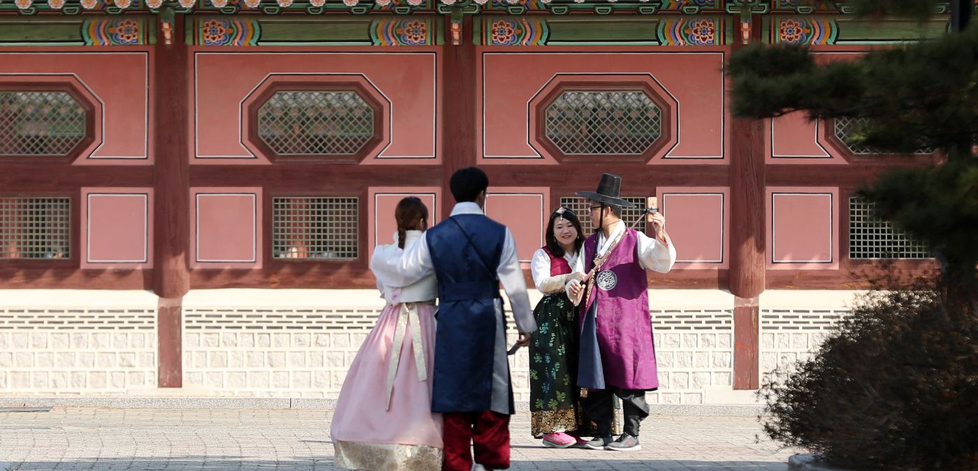 Visitors in rented hanbok photographing each other in front of a painted palace wall at Gyeongbokgung, Seoul